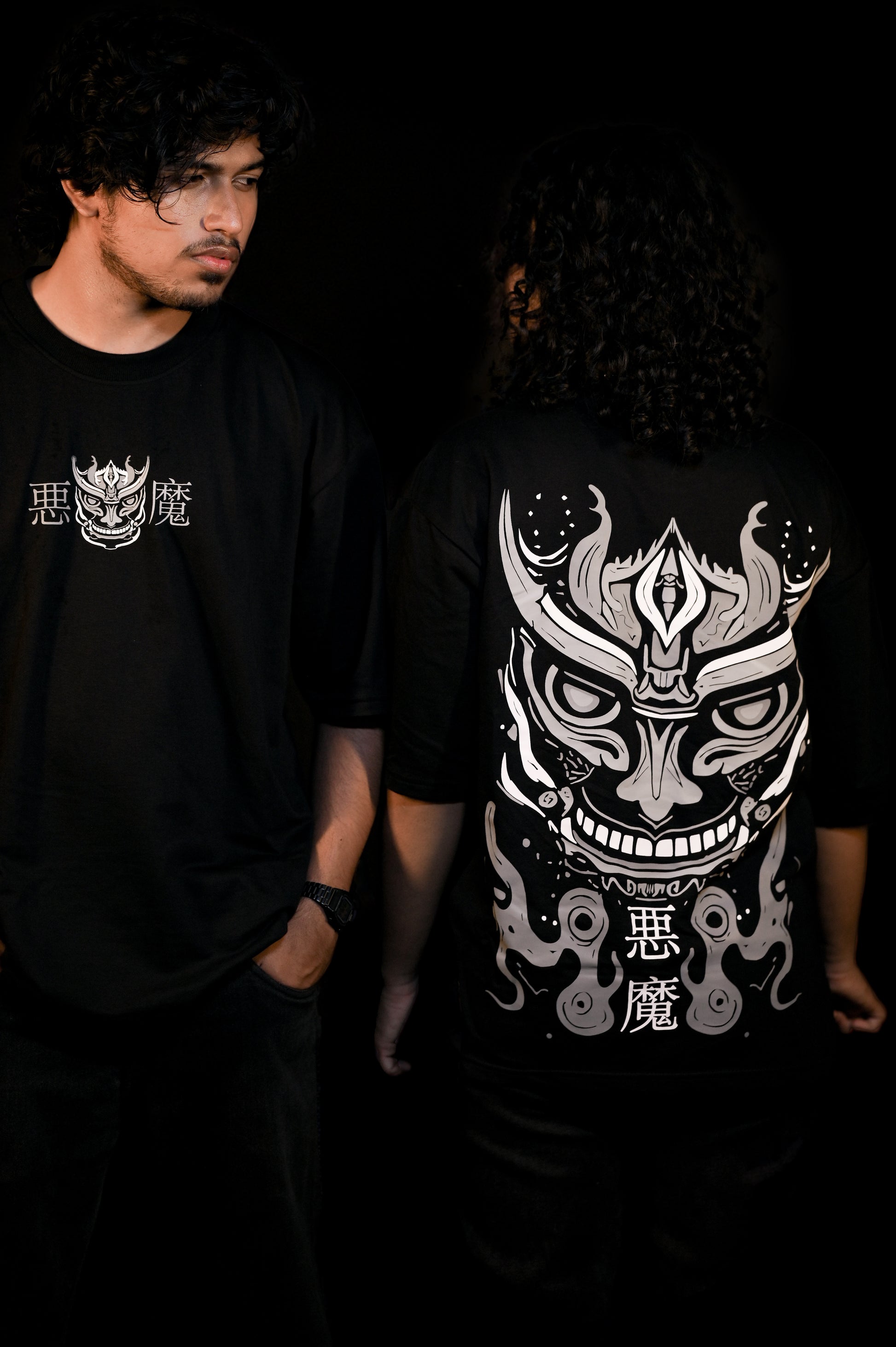 Two people wearing black t-shirts with white graphic designs on a dark background